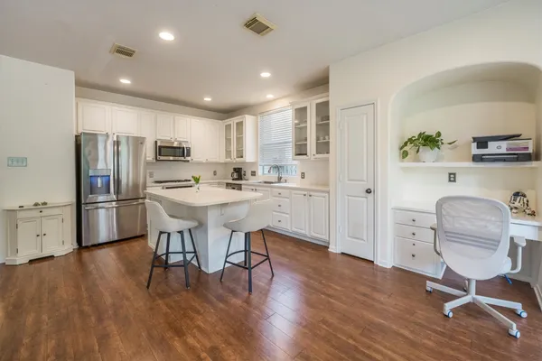 a kitchen with stainless steel appliances granite countertop a refrigerator a sink a stove a dining table and chairs with wooden floor