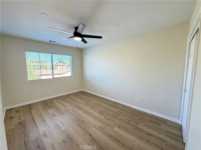 an empty room with wooden floor ceiling fan and windows