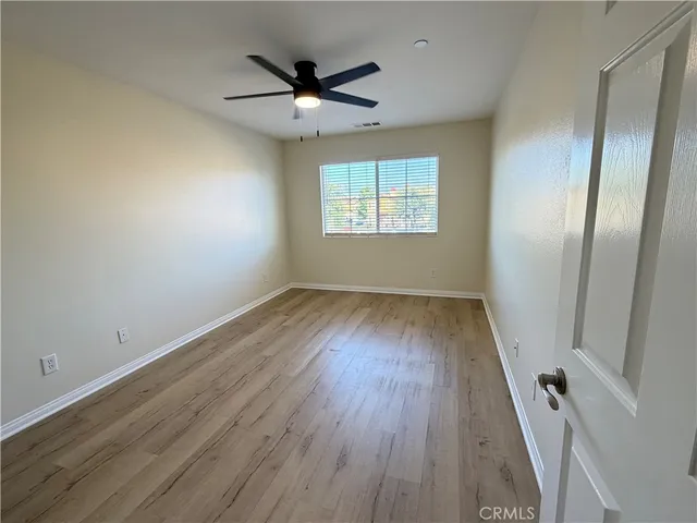 an empty room with wooden floor fan and windows