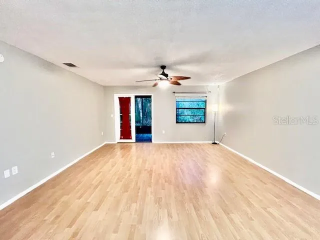 a view of an empty room with wooden floor and a ceiling fan