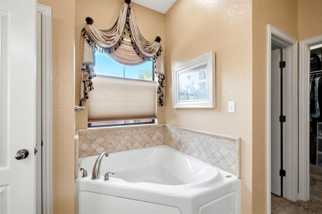 600 Aspen Street Pilot Point, TX 76258 - Photo 12 of 39 White corner soaking tub with chrome fixtures, surrounded by a mosaic tile backsplash and a neutral-toned wall finish
