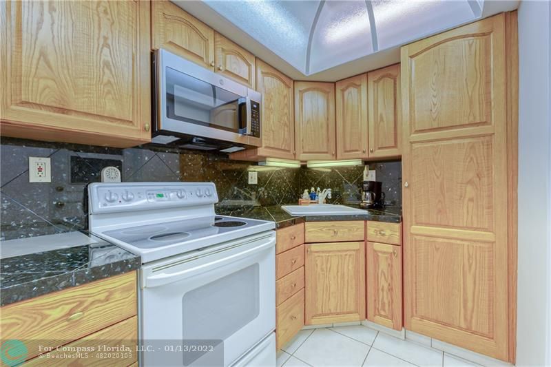 1210 North Riverside Drive, Unit 107 Pompano Beach, FL 33062 - Photo 6 of 29 a kitchen with white cabinets and white appliances