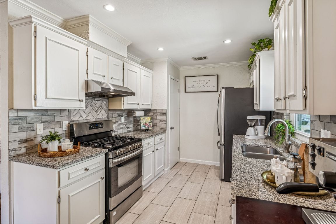 5502 Porsche Lane Austin, TX 78749 - Photo 15 of 32 Kitchen with stainless steel appliances, light stone counters, tasteful backsplash, white cabinetry, and crown molding