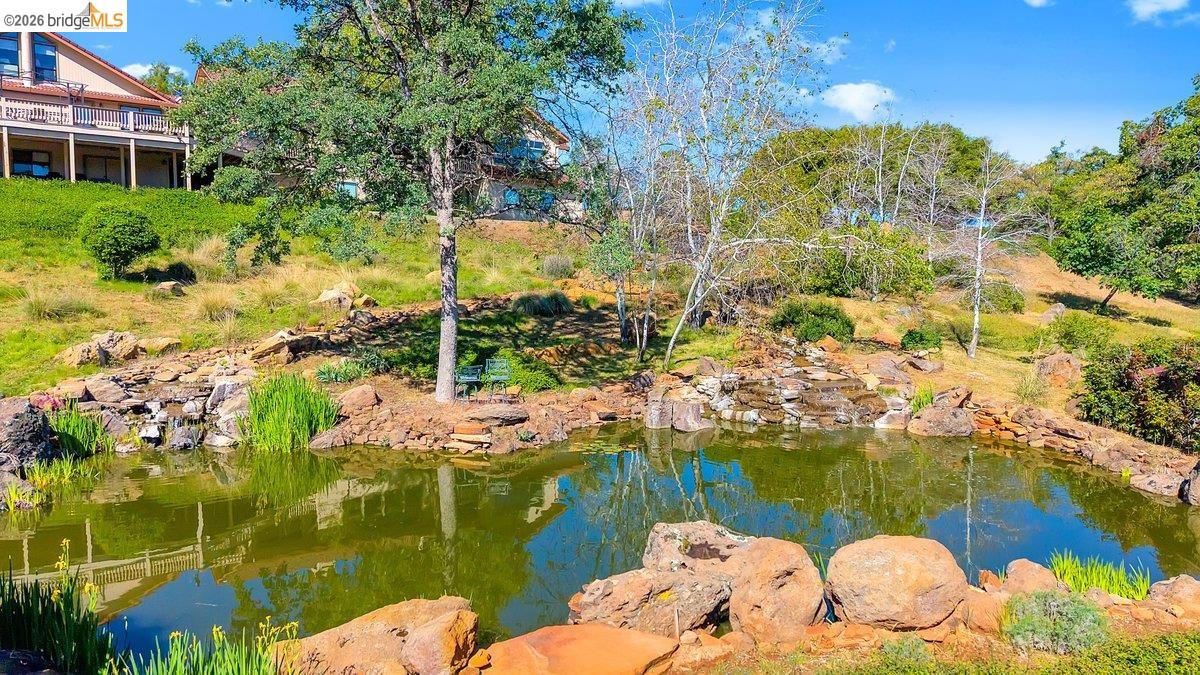13700 Clements Road Groveland, CA 95321 - Photo 88 of 93 Expansive pond with rock-lined edges, a cascading waterfall feature, surrounding natural landscaping, and mature trees