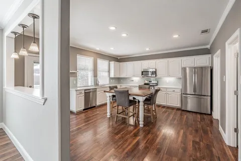 a kitchen with stainless steel appliances a refrigerator a stove a sink dishwasher and a dining table with wooden floor