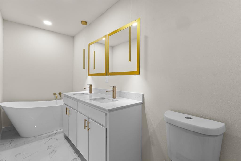 907 Pinson Road Forney, TX 75126 - Photo 16 of 35 Contemporary bathroom featuring a freestanding tub, double vanity with white cabinetry, gold-toned hardware, and marble-look flooring