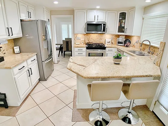 a kitchen with stainless steel appliances granite countertop a sink a stove a refrigerator cabinets and chairs
