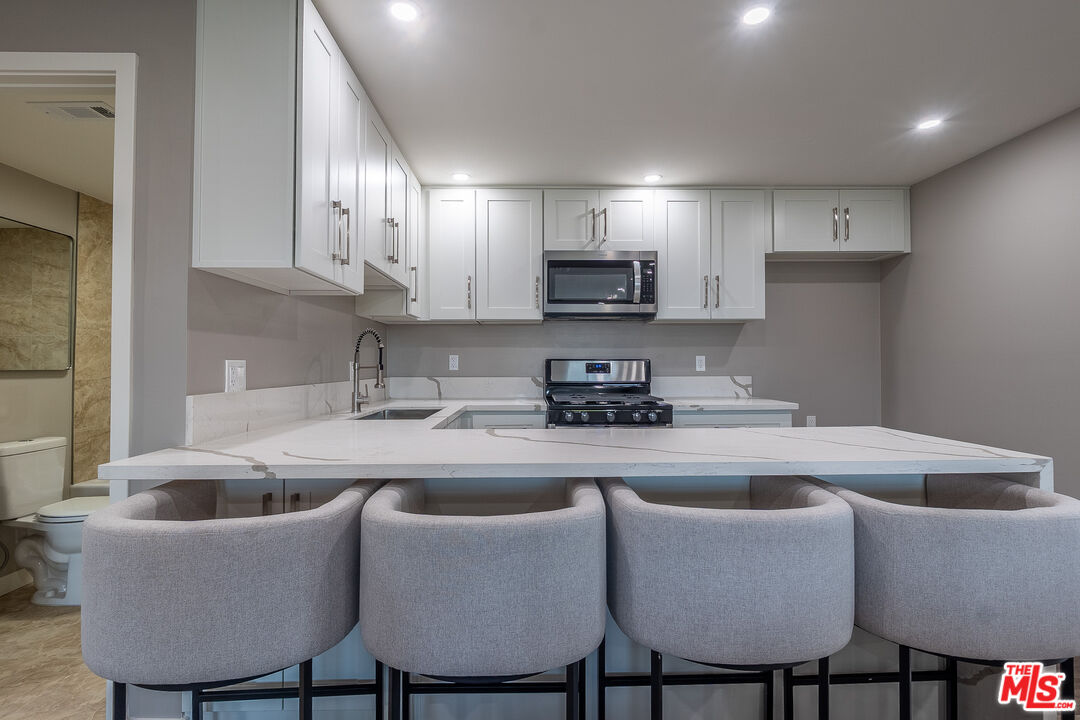 20456 Strathern Street Winnetka, CA 91306 - Photo 31 of 37 a kitchen with stainless steel appliances granite countertop a sink a stove a refrigerator with white cabinets and couches