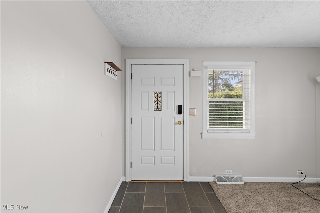Foyer entrance featuring baseboards, visible vents, and a textured ceiling