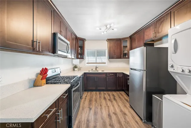 a kitchen with stainless steel appliances granite countertop a refrigerator a sink dishwasher a stove and white countertops with wooden floor