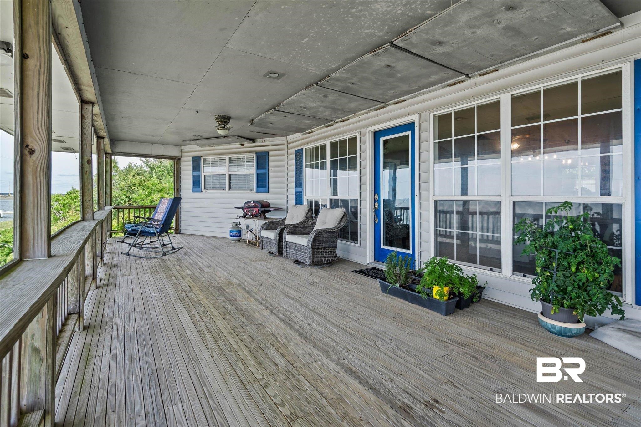 9100 Shell Belt Road Coden, AL 36523 - Photo 7 of 38 Expansive wood-finish deck with white siding, blue-shuttered windows, and a vibrant blue entry door