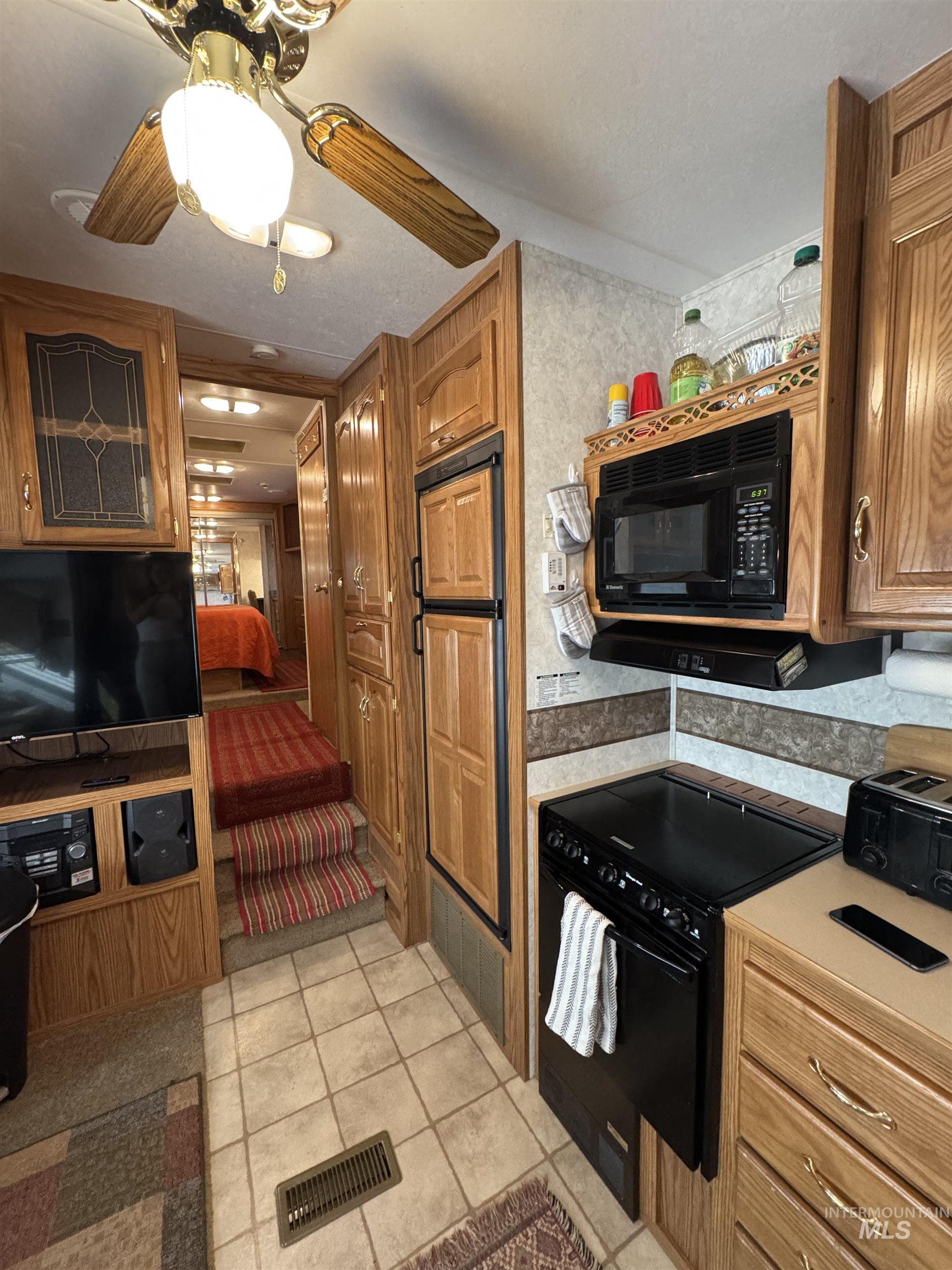 29 B Street Cascade, ID 83611 - Photo 8 of 24 Kitchen with black appliances, brown cabinets, ceiling fan, light tile patterned flooring, and light countertops