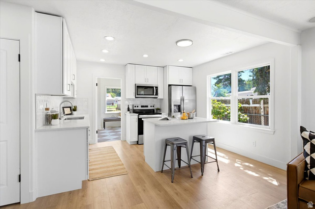 307 Flint Street Layton, UT 84041 - Photo 4 of 13 Bright kitchen featuring white cabinetry, stainless steel appliances, a center island with seating, wood-finish flooring, and ample natural light from multiple windows