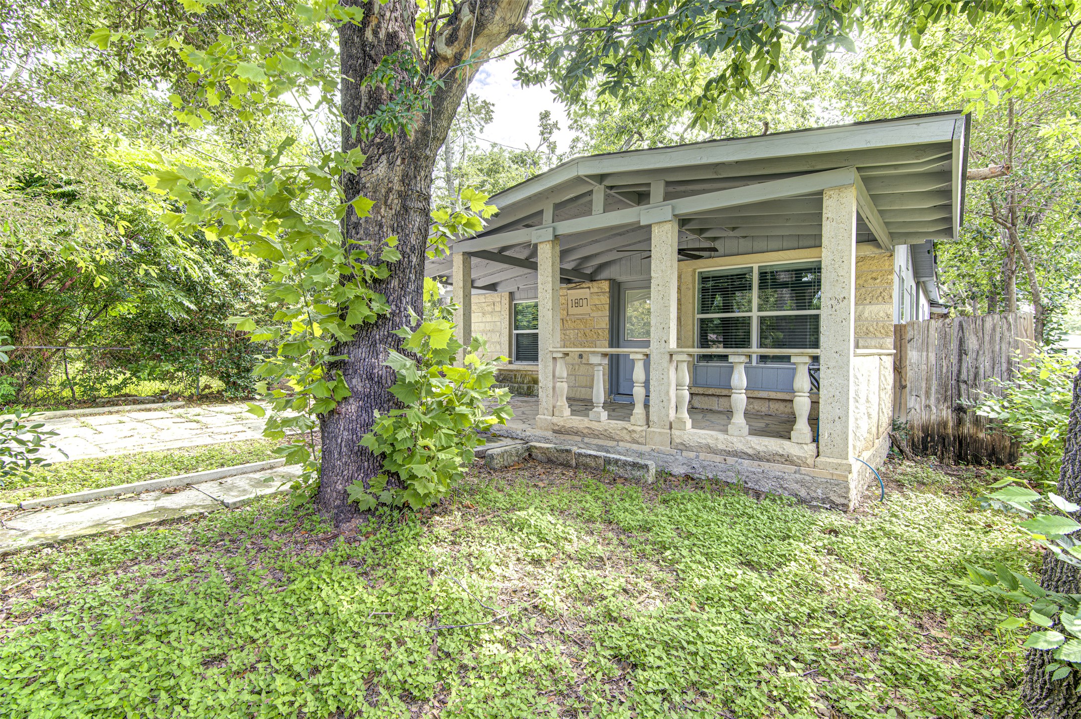 1807 San Jose Street Georgetown, TX 78626 - Photo 3 of 21 A charming front porch with stone balusters awaits, nestled amongst mature trees and verdant landscaping.