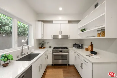 a kitchen with a sink dishwasher a stove and white cabinets with wooden floor