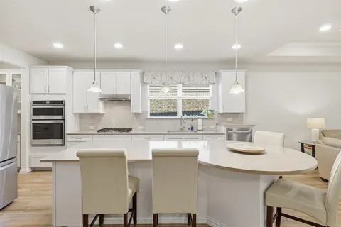 a kitchen with kitchen island granite countertop a sink a stove a refrigerator cabinets and chairs