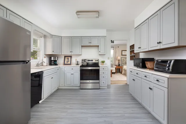 a kitchen with granite countertop a refrigerator oven a sink dishwasher and white cabinets with wooden floor