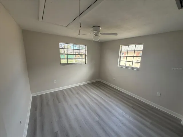an empty room with wooden floor windows and fan