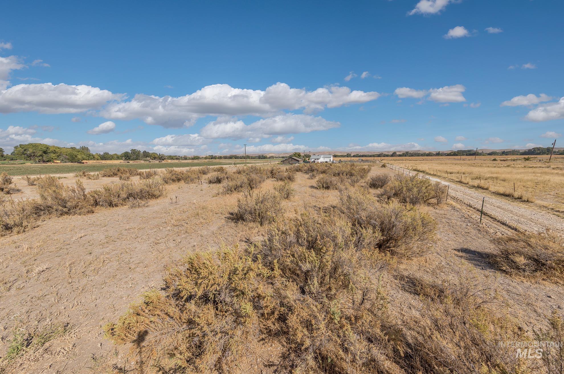 4631 Rolland Road Ontario, OR 97914 - Photo 35 of 43 Expansive property featuring a gravel road and distant structures, set against a backdrop of open terrain and a clear sky with scattered clouds