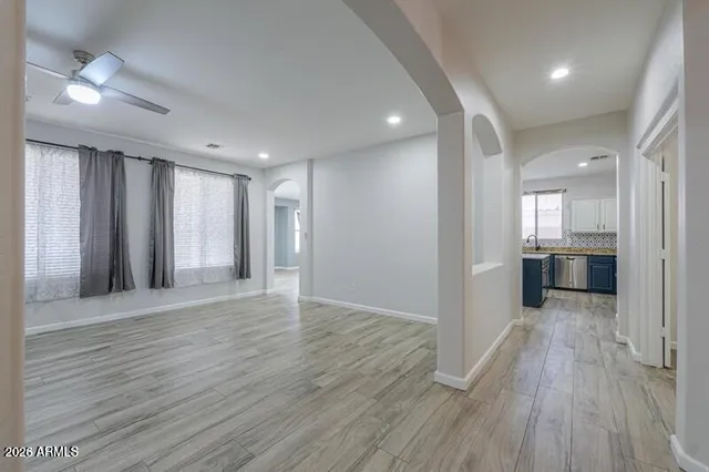 an empty room with wooden floor kitchen view and windows