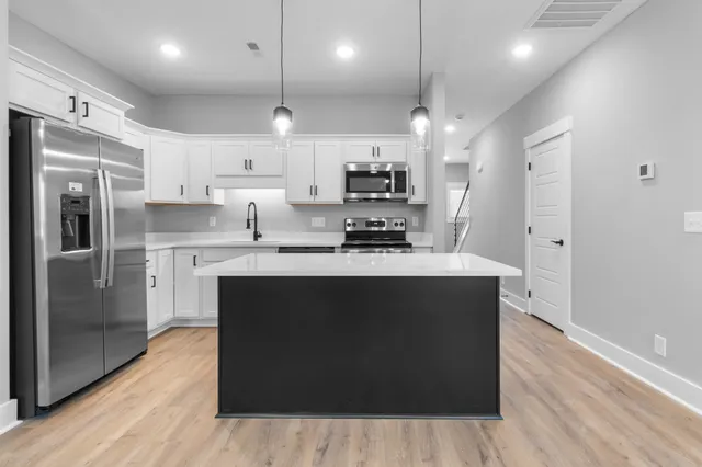 a kitchen with stainless steel appliances granite countertop a refrigerator a sink dishwasher a stove and white cabinets with wooden floor