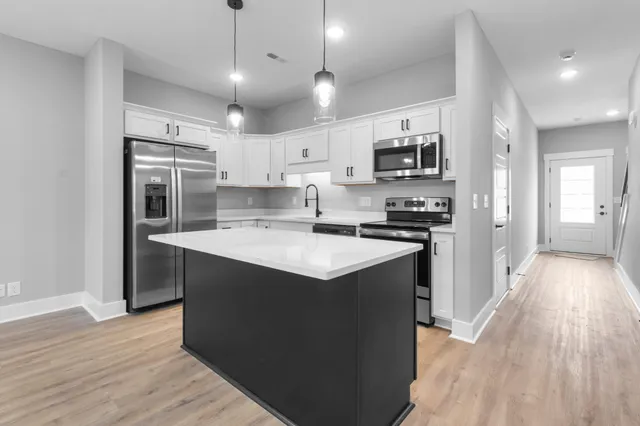 a kitchen with stainless steel appliances granite countertop a stove top oven a refrigerator a sink and dishwasher with wooden floor