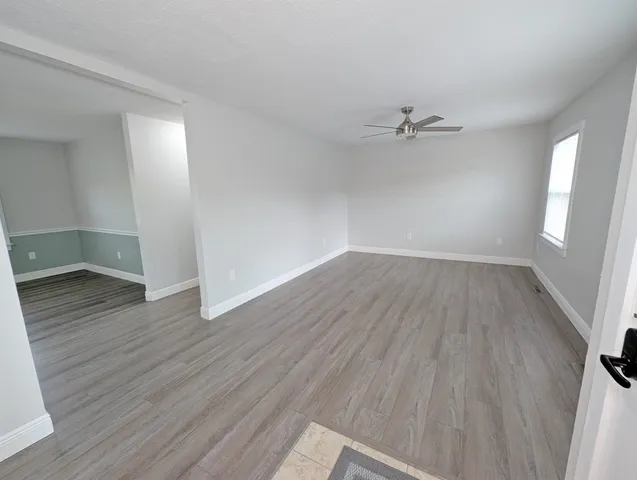 an empty room with wooden floor ceiling fan and windows