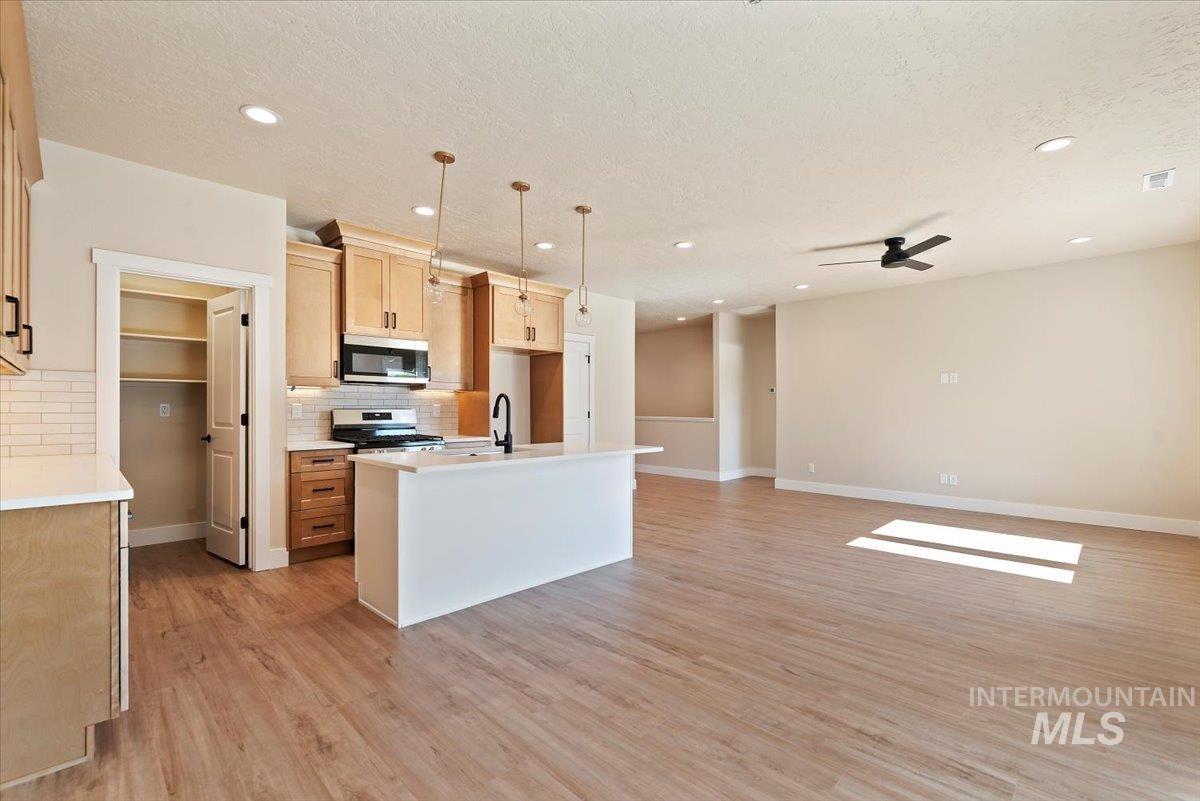 1300 Birch Street Parma, ID 83660 - Photo 6 of 25 Kitchen with a center island with sink, tasteful backsplash, light wood finished floors, appliances with stainless steel finishes, and a textured ceiling