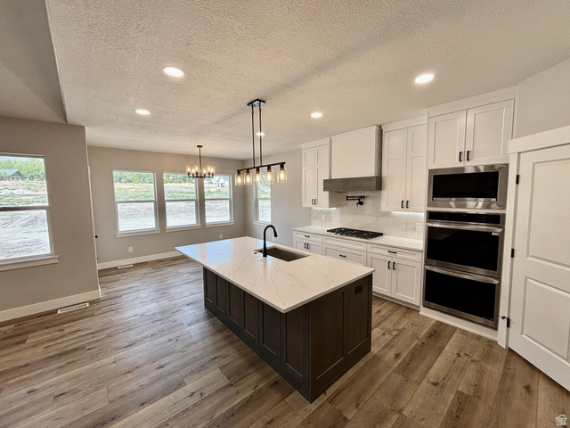 1184 West 3250 North Ogden, UT 84414 - Photo 12 of 69 Spacious open-concept kitchen featuring a dark-toned island with a white countertop and integrated sink, light wood-finish flooring, white cabinetry with black hardware, and stainless steel double ovens
