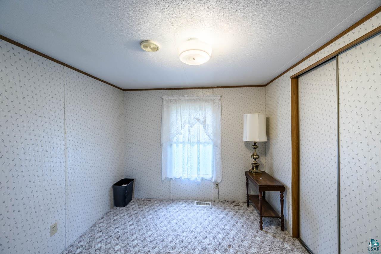 705 4th Street North Biwabik, MN 55708 - Photo 14 of 29 Carpeted room with patterned wallpaper, featuring a ceiling-mounted light fixture, a window with sheer curtains, and a built-in closet with wood-finish trim