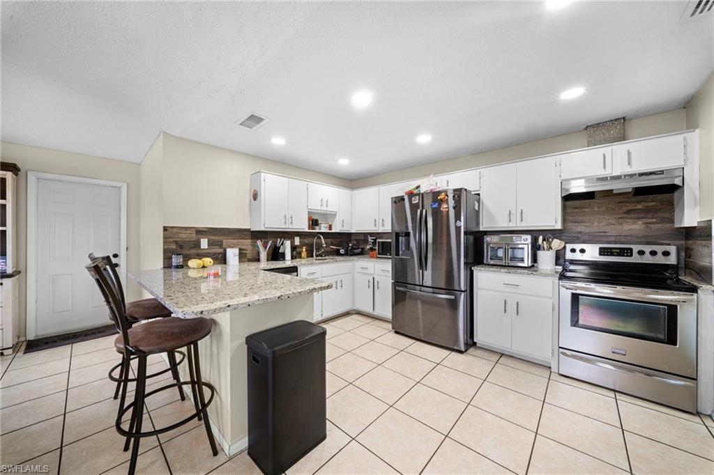7289 Barragan Road Fort Myers, FL 33967 - Photo 5 of 18 Kitchen featuring white cabinetry, light-toned tile flooring, recessed lighting, wood-paneled backsplash, and a granite-look island with breakfast bar seating