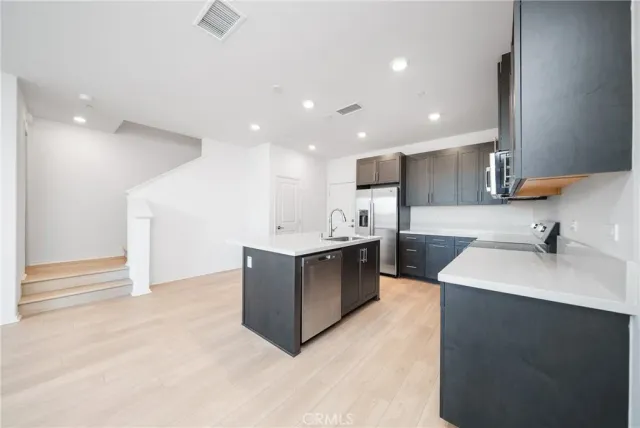 a large kitchen with a large counter top a sink stainless steel appliances and cabinets