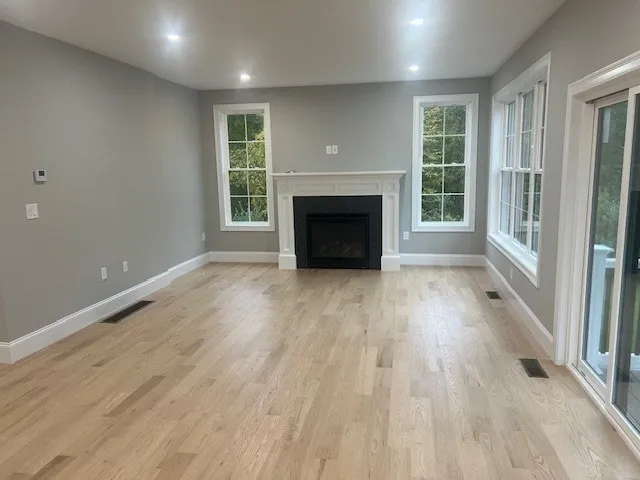 an empty room with wooden floor fireplace and windows