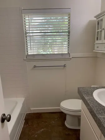 a bathroom with a granite countertop toilet a sink and a window