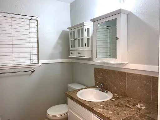 a bathroom with a granite countertop sink toilet a mirror and window