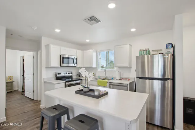 a kitchen that has a refrigerator a stove a sink and a dining table with wooden floor