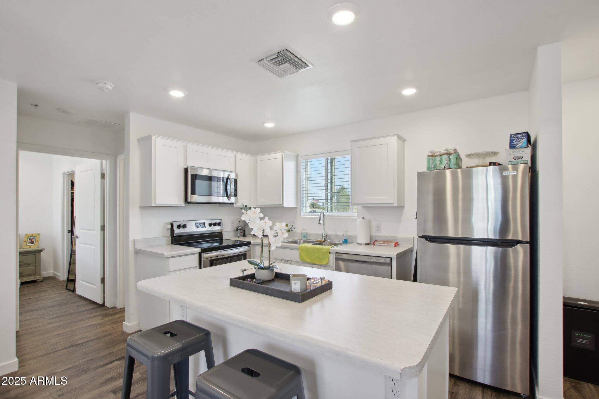 12925 West Greenway Road, Unit 5 El Mirage, AZ 85335 - Photo 6 of 30 a kitchen that has a refrigerator a stove a sink and a dining table with wooden floor