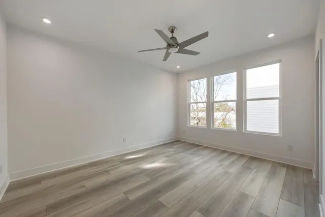 an empty room with wooden floor fan and windows
