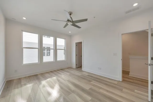 an empty room with wooden floor fan and windows