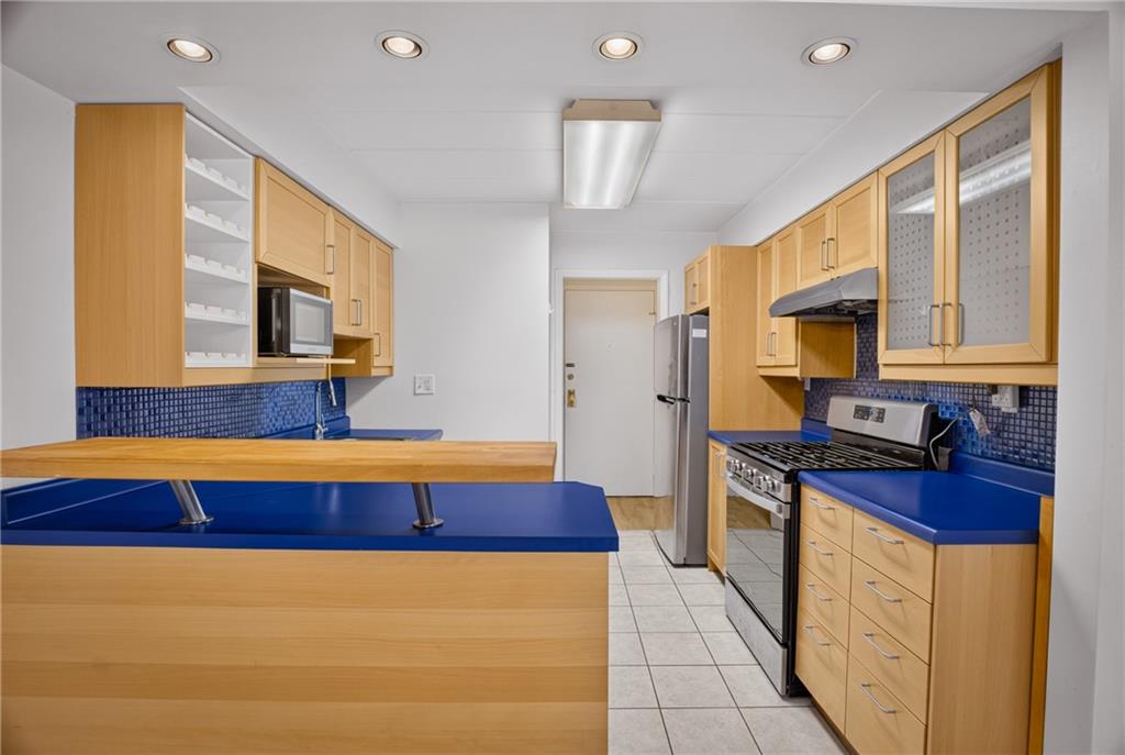 5 Bayard Road, Unit 418 Pittsburgh, PA 15213 - Photo 31 of 45 Bright and full of character, the kitchen pairs warm light oak cabinetry with select open shelving, creating an inviting blend of style and functionality. A striking blue countertop and matching backsplash add a distinctive pop of color, giving the space a fresh, cheerful personality that's perfect for everyday living.