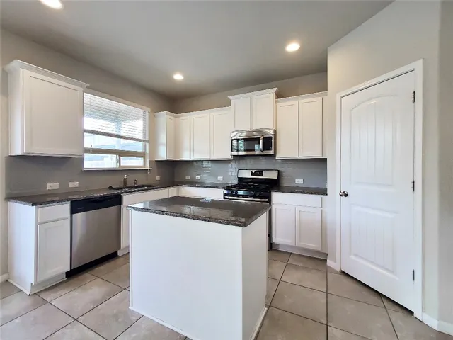 a kitchen with stainless steel appliances granite countertop white cabinets a sink a stove a microwave and a refrigerator