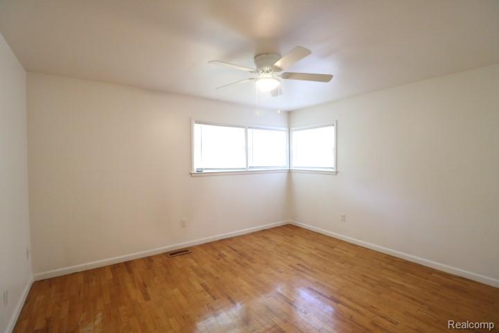 1404 South Graham Road Flint, MI 48532 - Photo 11 of 17 Room featuring wood-finish flooring, two large windows, a ceiling fan with integrated lighting, and white walls