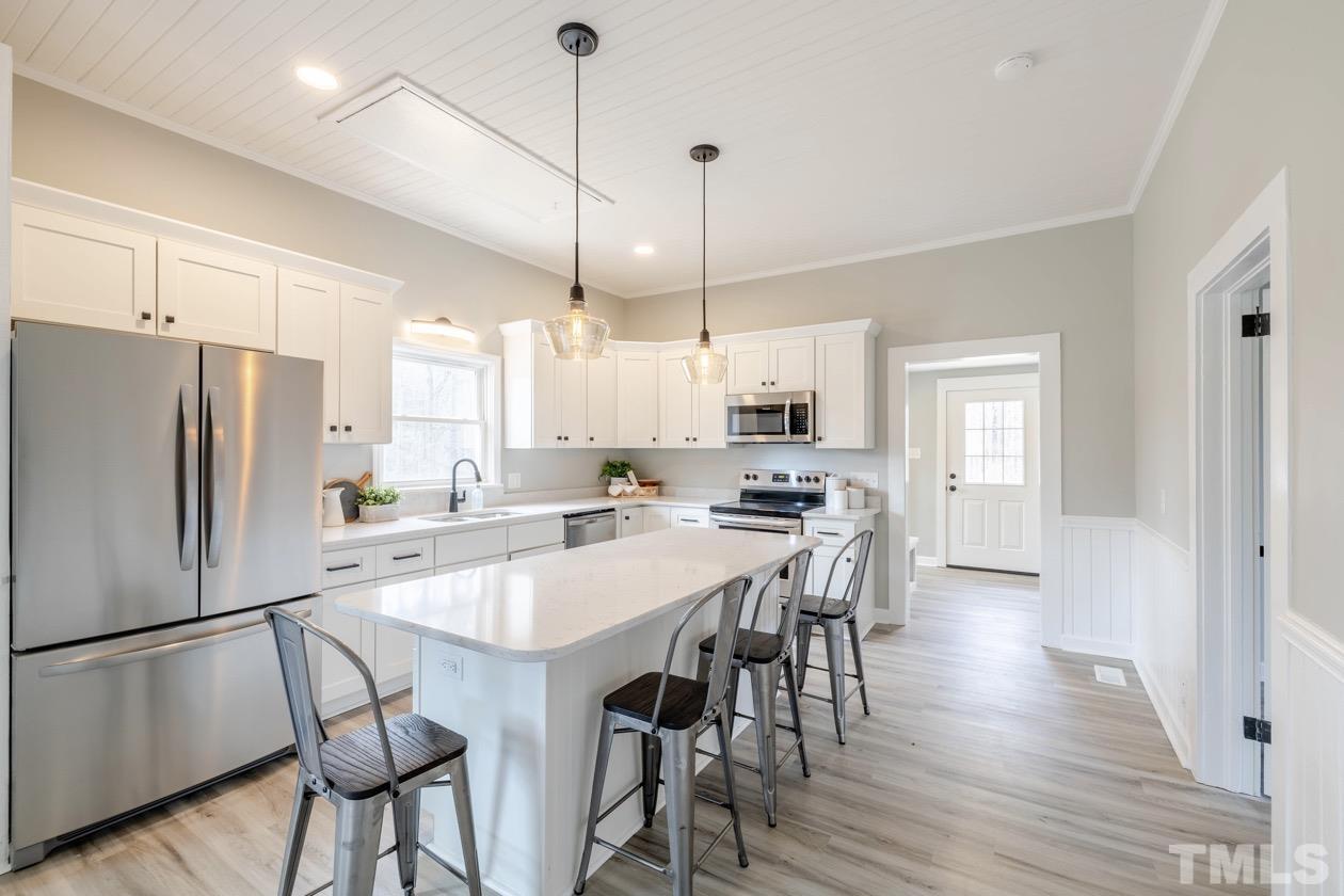7311 Stagville Road Bahama, NC 27503 - Photo 5 of 37 a kitchen with stainless steel appliances a refrigerator a stove a kitchen island a dining table and chairs with wooden floor