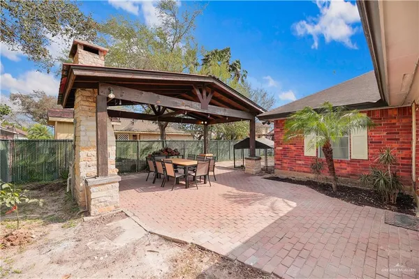 a view of a patio with a table and chairs under an umbrella with a barbeque grill and a small yard