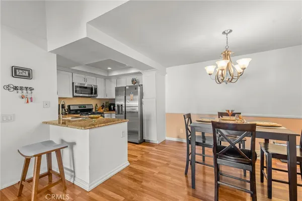 a kitchen with stainless steel appliances granite countertop a stove top oven a refrigerator a dining table and chairs with wooden floor