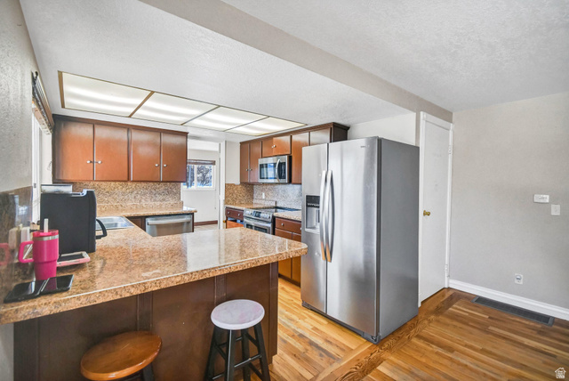 10 North Main Street Centerfield, UT 84622 - Photo 15 of 52 Kitchen featuring appliances with stainless steel finishes, a peninsula, light wood-type flooring, a kitchen breakfast bar, and backsplash