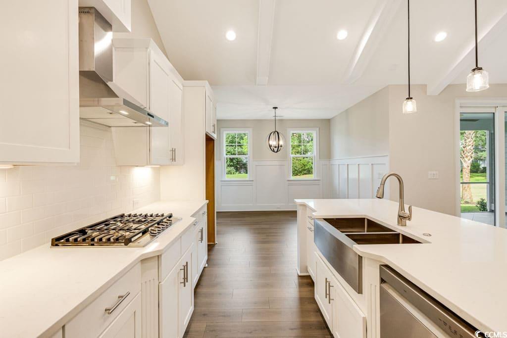 394 Sea Trail Drive West Sunset Beach, NC 28468 - Photo 14 of 40 Kitchen featuring beamed ceiling, white cabinets, wall chimney exhaust hood, stainless steel appliances, and pendant lighting