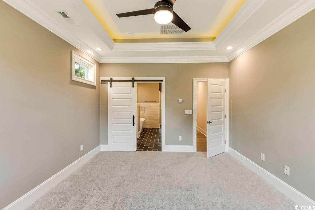 394 Sea Trail Drive West Sunset Beach, NC 28468 - Photo 18 of 40 Unfurnished bedroom featuring carpet floors, a barn door, a tray ceiling, crown molding, and connected bathroom