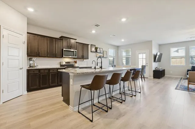a kitchen with stainless steel appliances kitchen island granite countertop a stove a refrigerator a sink a dining table and chairs with wooden floor