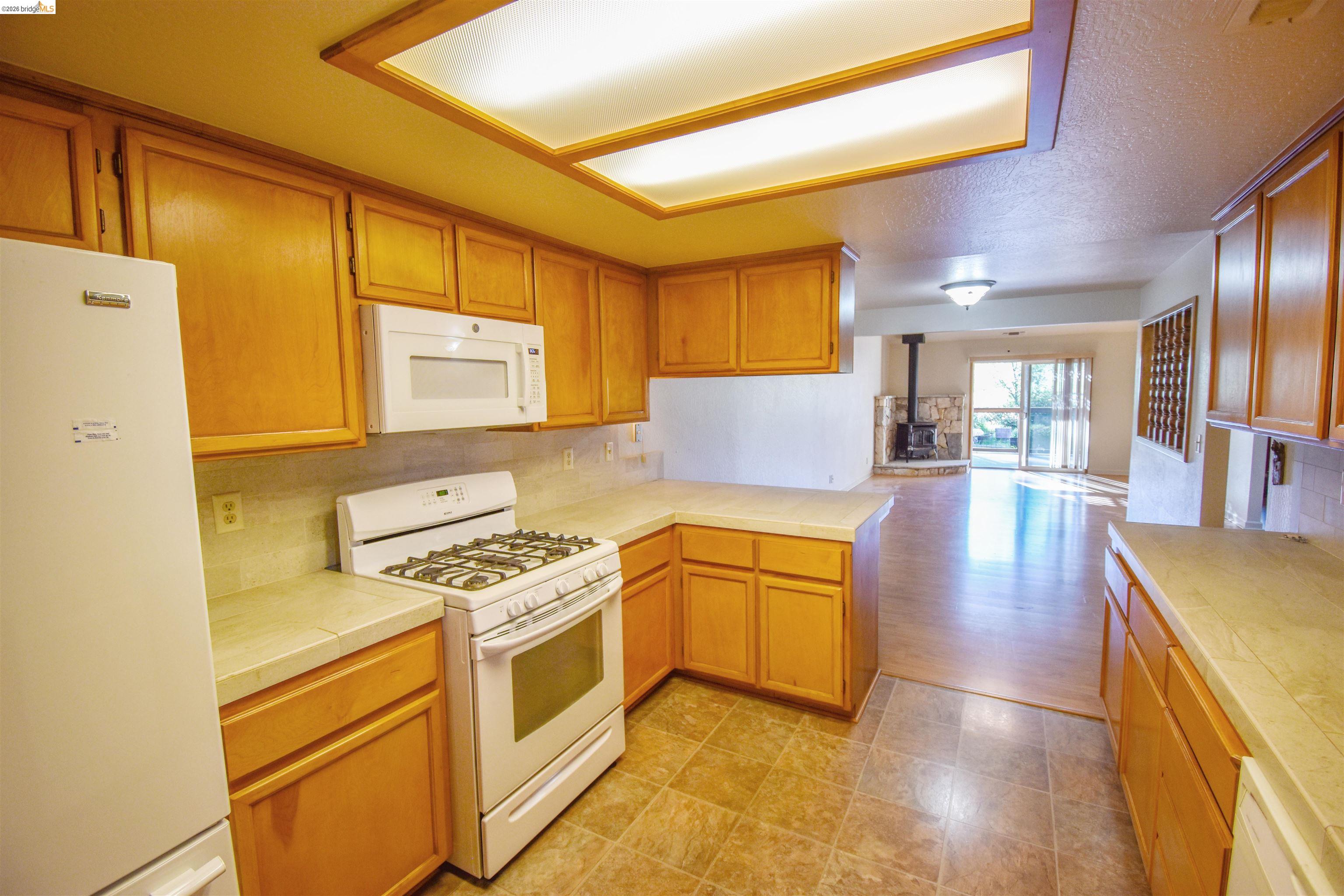 23685 Marble Quarry Road, Unit 22 Columbia, CA 95310 - Photo 33 of 33 Kitchen with white appliances, a wood stove, a peninsula, open floor plan, and backsplash